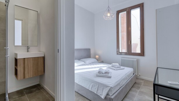 A modern bedroom with a bed, bedside table, and a window. - Suite Zucchero | BluesHouse Carracci (Bologna)