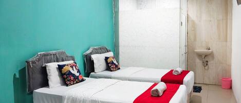 A room with two beds, each with a red blanket and a pillow with a floral design. There is a white sink and a small trash bin in the corner.