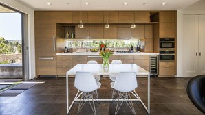 A modern kitchen with a central island, white chairs, and a view of the outdoors. - Healdsburg Modern Retreat - Pool, Views & Design (Healdsburg)