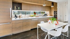 A modern kitchen with wooden cabinets, a white countertop, and a dining area with a white table and chairs. - Healdsburg Modern Retreat - Pool, Views & Design (Healdsburg)