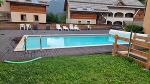 Une piscine rectangulaire dotée d’une terrasse en bois, entourée de chaises longues blanches et d’une clôture en bois.