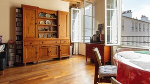 Ein Zimmer mit Holzboden, einem großen Holzschrank mit Regalen, einem Esstisch mit Stuhl und einem Fenster mit geöffneter Tür.