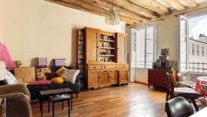 Ein gemütliches Wohnzimmer mit Holzböden, einer Couch mit Kissen, einem Holzschrank mit Regalen und einem Essbereich mit Tisch und Stühlen.