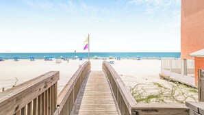 A wooden boardwalk leading to a beach with umbrellas and a flag.