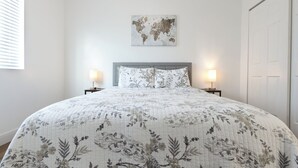 Ein ordentlich bezogenes Bett mit floralem Bettzeug, eine Weltkarte an der Wand und zwei Nachttischlampen.