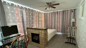 A living room with a fireplace, a ceiling fan, a TV on a stand, and a chair with a floral cushion. - beaches house near by beach (Holiday)