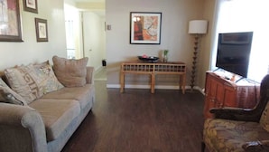 A living room with a sofa, a wooden coffee table, a patterned armchair, and a television on a cabinet. - beaches house near by beach (Holiday)