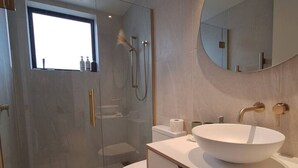 Un bagno moderno con doccia vetrata, un water bianco e un ampio lavabo ovale con rubinetto dorato.