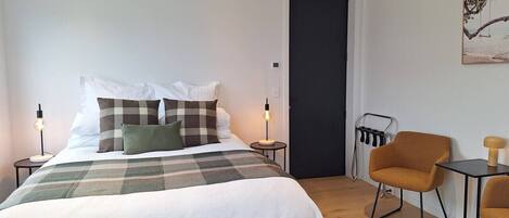 A bedroom with a bed, a chair, a table, and a door.