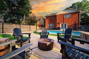 Un patio al aire libre con sillas Adirondack, una fogata y una piscina.