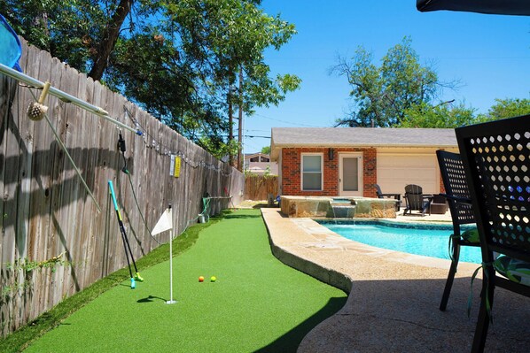 Un patio trasero con piscina, césped artificial y valla de madera.