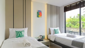 A hotel room with two beds, a bedside table with a kettle, a small artwork on the wall, and a window with a view of greenery. - Mono Coliving Kota Tua, Jakarta (Jakarta)