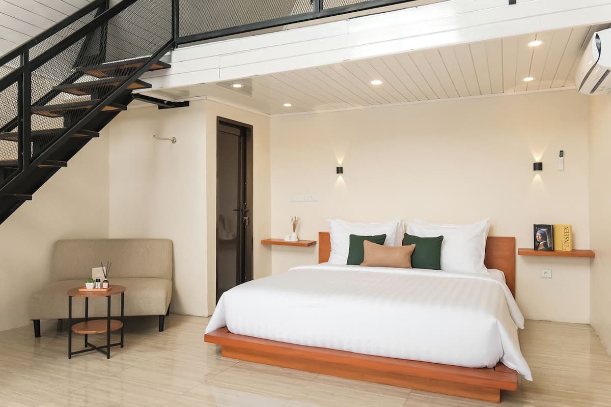Une chambre d’hôtel moderne avec un grand lit, une petite table ronde, un canapé et un escalier.