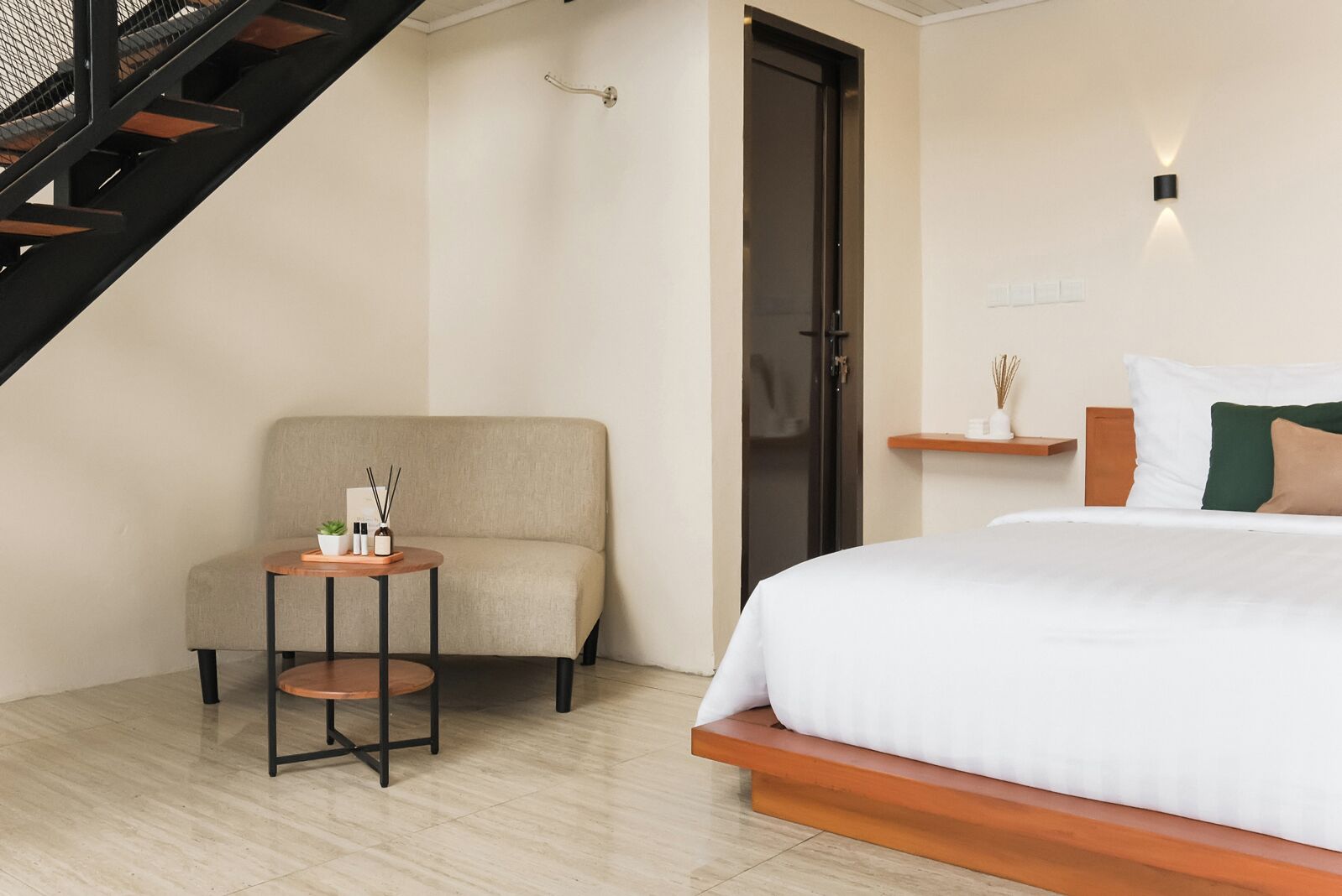 A bedroom with a bed, a chair, a small table, a staircase, and a door.