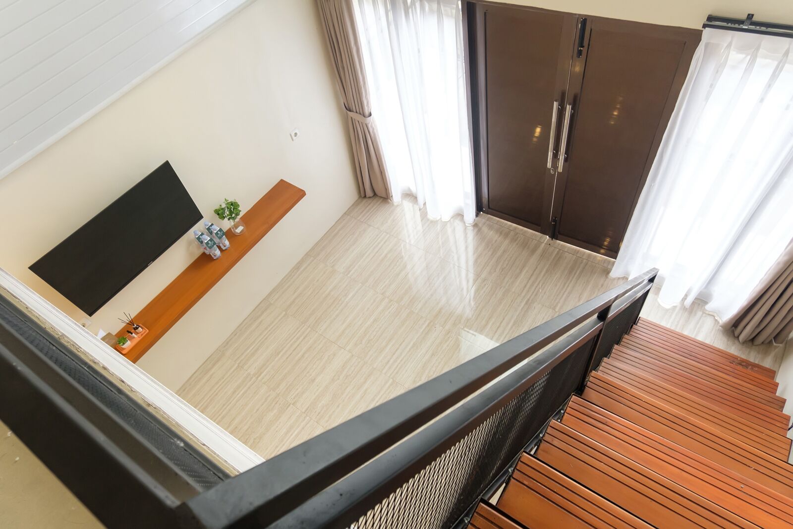Un'ampia stanza con un'ampia finestra, pavimento in legno, TV a schermo piatto e una panca in legno.