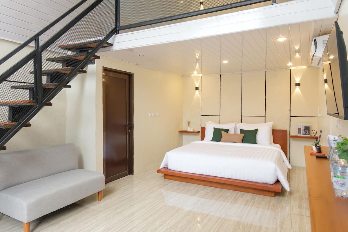 Une chambre moderne avec un lit, un canapé, un escalier et une petite table sur laquelle est posée une plante.