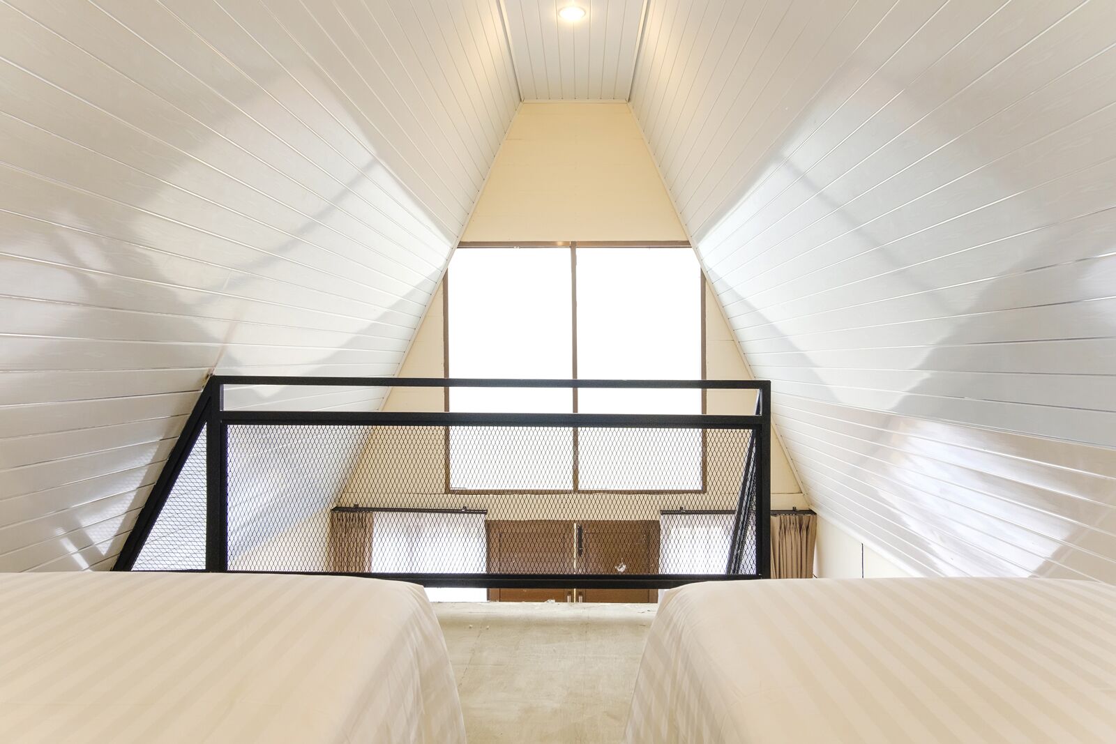 A narrow attic bedroom with a sloped ceiling, a black metal railing, and a large window providing natural light.