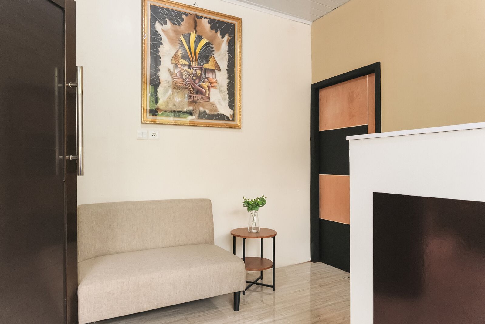 Une pièce comprenant un canapé, une petite table sur laquelle est posé un vase, une œuvre d’art encadrée au mur et une porte dotée d’un cadre noir.