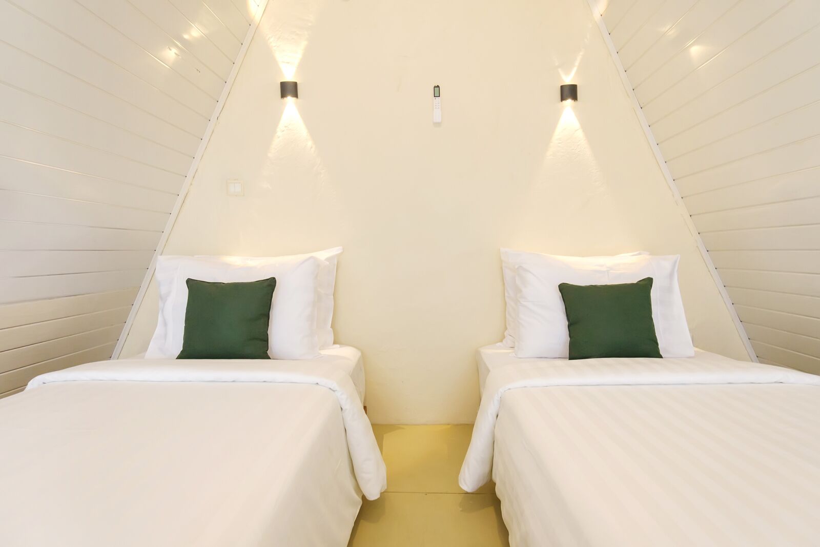 Een kamer met twee bedden, elk voorzien van witte beddengoed en groene kussens, en een lichtgekleurde vloer.