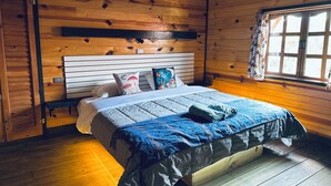 A wooden cabin-style bedroom with a bed, pillows, and a window with curtains. - Embellupe Lodging (San José del Pacífico)