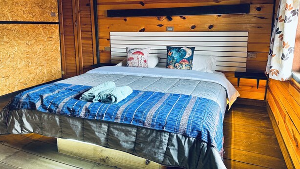 A wooden cabin bedroom with a bed, pillows, and a bench. - Embellupe Lodging (San José del Pacífico)