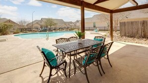 A covered patio with a pool, outdoor furniture, and a view of a residential area.