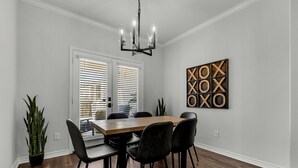 A dining area with a wooden table, black chairs, a chandelier, and a wall-mounted artwork.