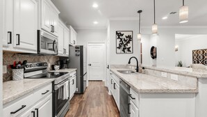 A modern kitchen with white cabinetry, stainless steel appliances, a granite countertop, and pendant lighting.