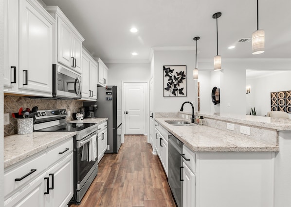 A modern kitchen with white cabinetry, stainless steel appliances, a granite countertop, and pendant lighting. - Casa Buena Vista Cozy Townhome Aggieland (College Station)