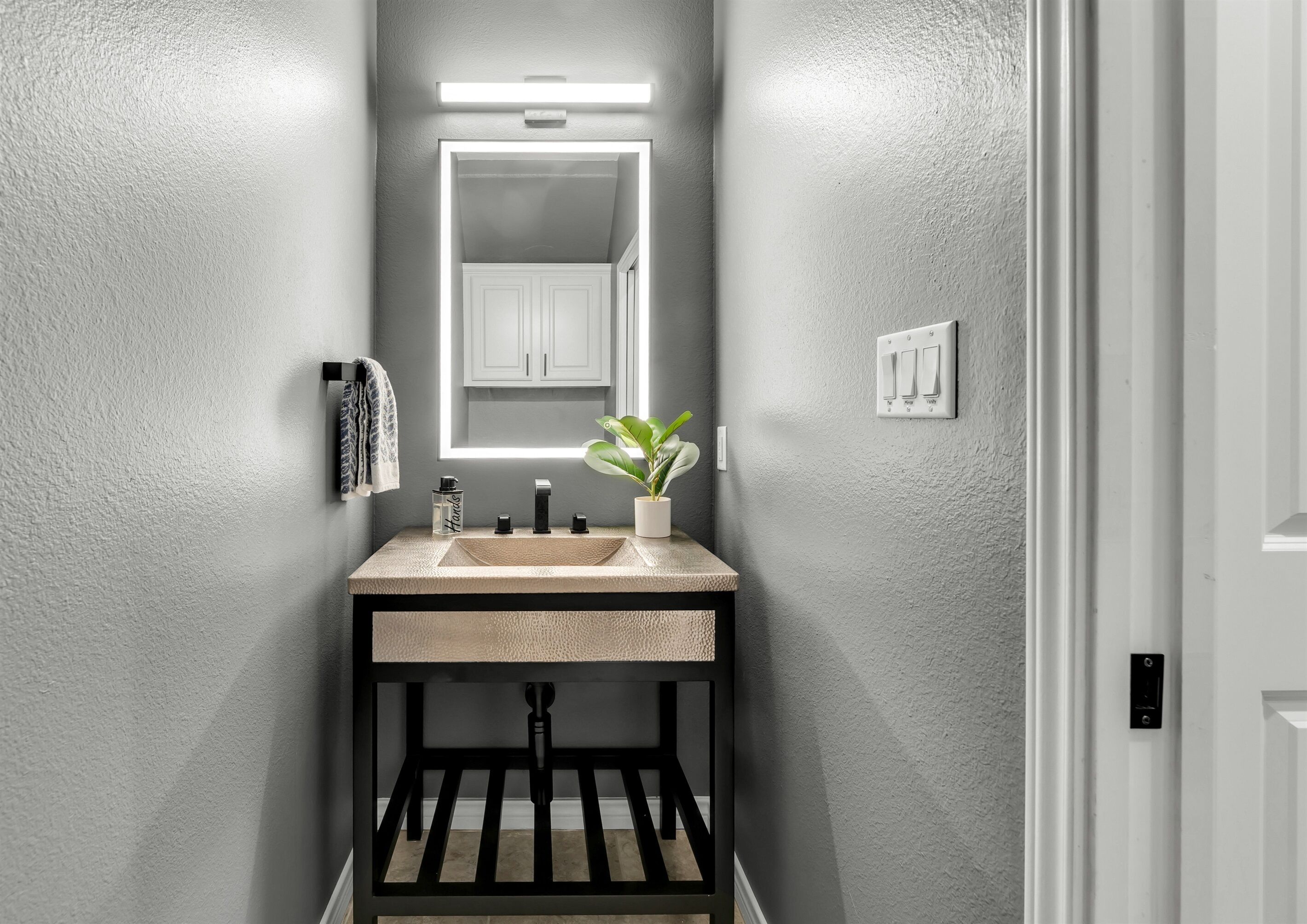 Casa de banho com lavatório moderno, espelho e planta em vaso.