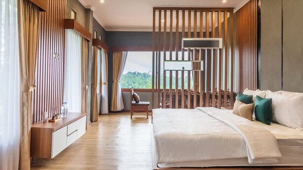 A modern bedroom with a large bed, a wooden desk, and a view of greenery outside. - Calma Coliving at Jatiluwih, Bali (Penebel)