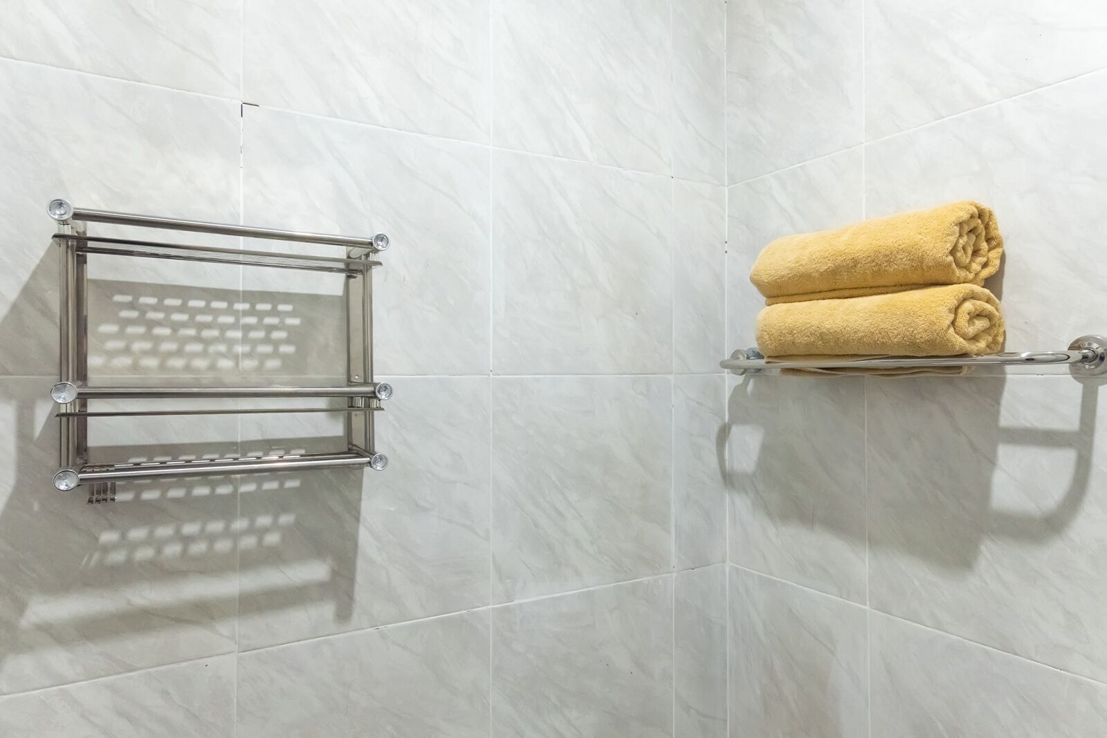 A bathroom with a glass towel rack and a towel shelf against a tiled wall.