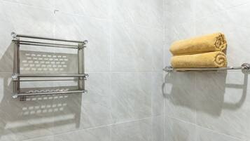 A bathroom with a glass towel rack and a towel shelf against a tiled wall.