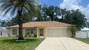 A single-story house with a garage, a front yard with a palm tree, and a clear sky. - Welcoming 3-bedroom house with pool and private yard (North Port)