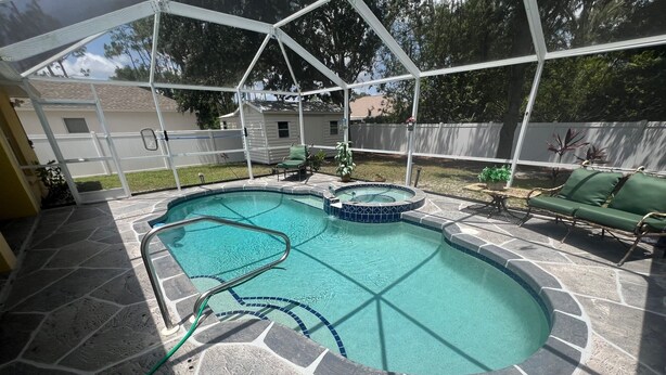 A backyard swimming pool with a stone deck, a hot tub, and a covered patio area. - Welcoming 3-bedroom house with pool and private yard (North Port)