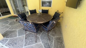 A round metal table with blue cushioned chairs, set on a stone patio against a yellow wall. - Welcoming 3-bedroom house with pool and private yard (North Port)