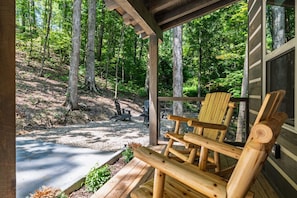 Eine Holzterrasse mit Adirondack-Stühlen, einem Betonweg und bewaldetem Hintergrund.