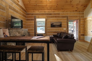 Ein rustikales Blockhaus-Interieur mit Kamin aus Stein, Holzwänden, einer Couch, einem Fernseher und einem Essbereich.