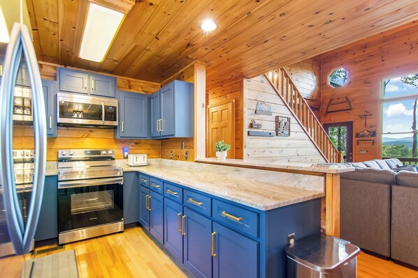 A modern kitchen with blue cabinets, stainless steel appliances, and a wooden ceiling.