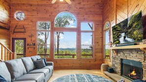 Interior acolhedor de uma cabana com lareira, um sofá e janelas amplas com uma vista panorâmica.
