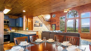 Interior de uma cabana de madeira, com área de jantar, cozinha e escada para um mezanino.