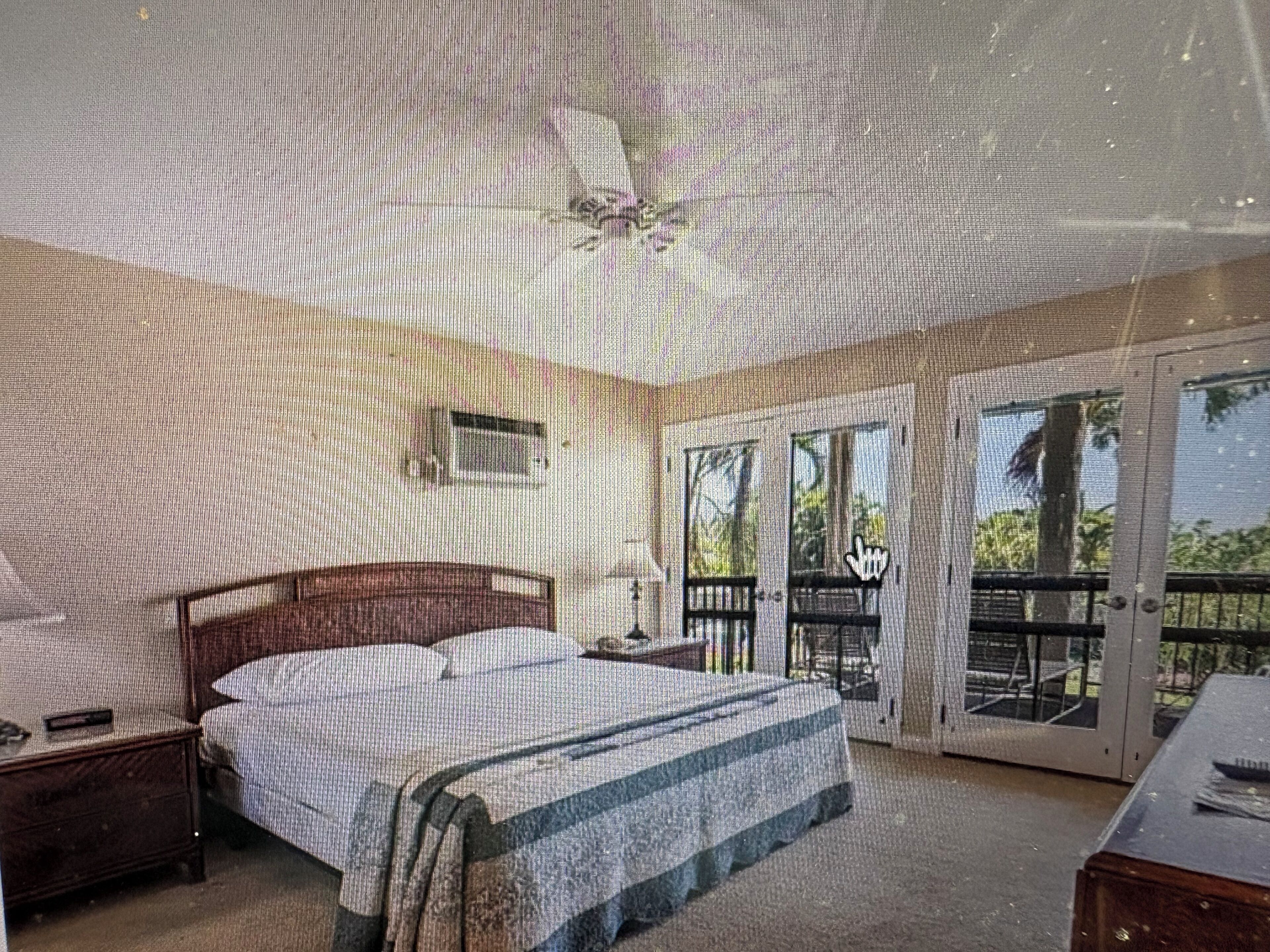 A bedroom with a bed, a nightstand, a desk, a chair, and a balcony with a railing.