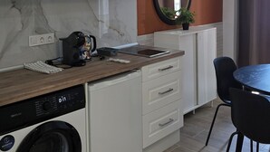 Una cocina moderna con armarios blancos, microondas integrado, cafetera y lavadora.