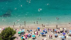 A beach with people swimming and sunbathing, umbrellas, and beach chairs. - Mediterranean Horizon (Villefranche-sur-Mer)