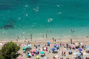Una playa con gente nadando y tomando el sol, sombrillas y sillas de playa.