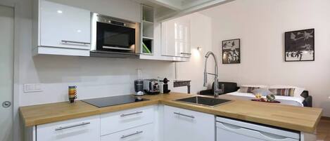 A modern kitchen with white cabinets, a stainless steel microwave, and a dishwasher. There is a wooden countertop and a sink.