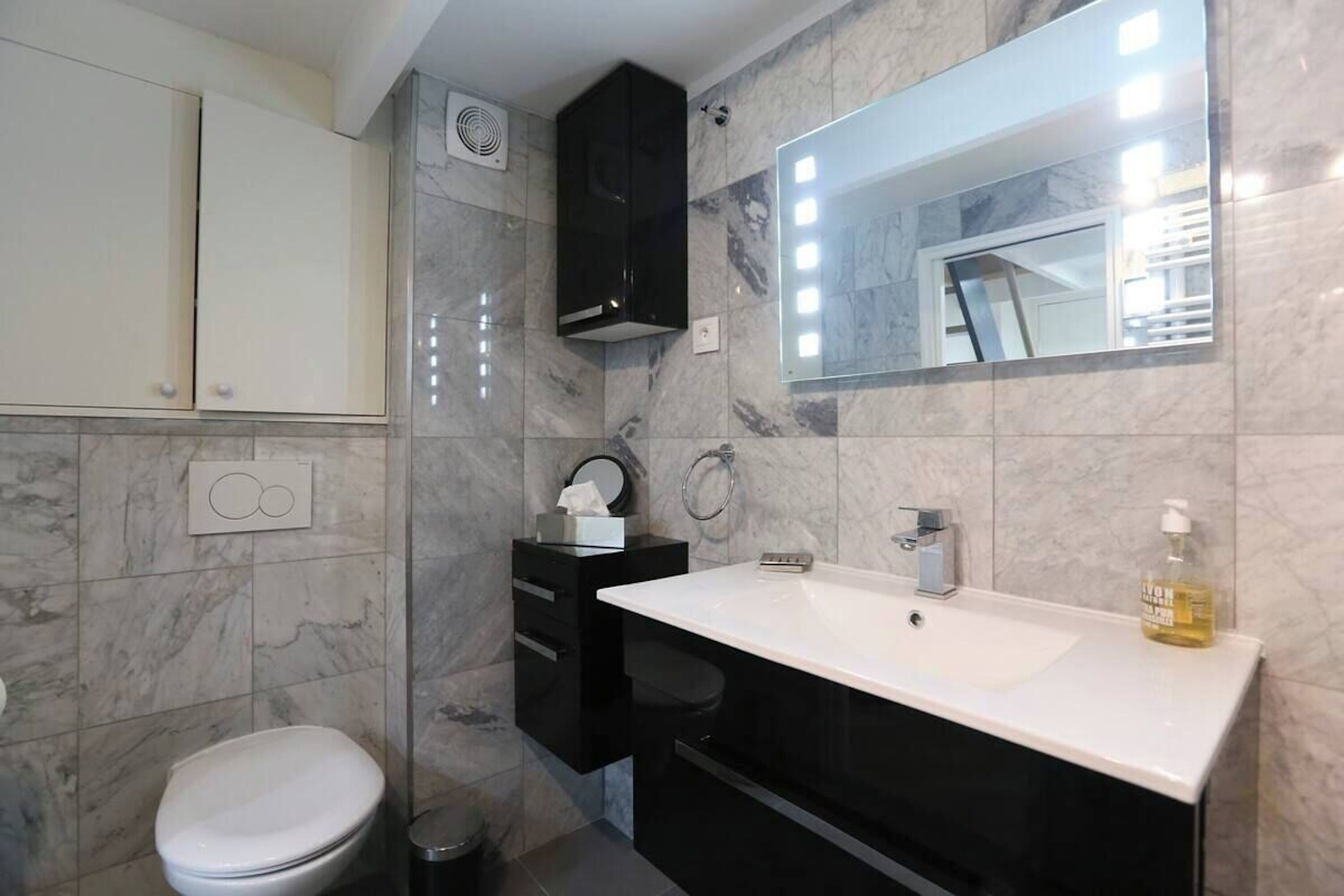 Un baño moderno con inodoro blanco, muebles negros, un espejo grande y un lavabo blanco.