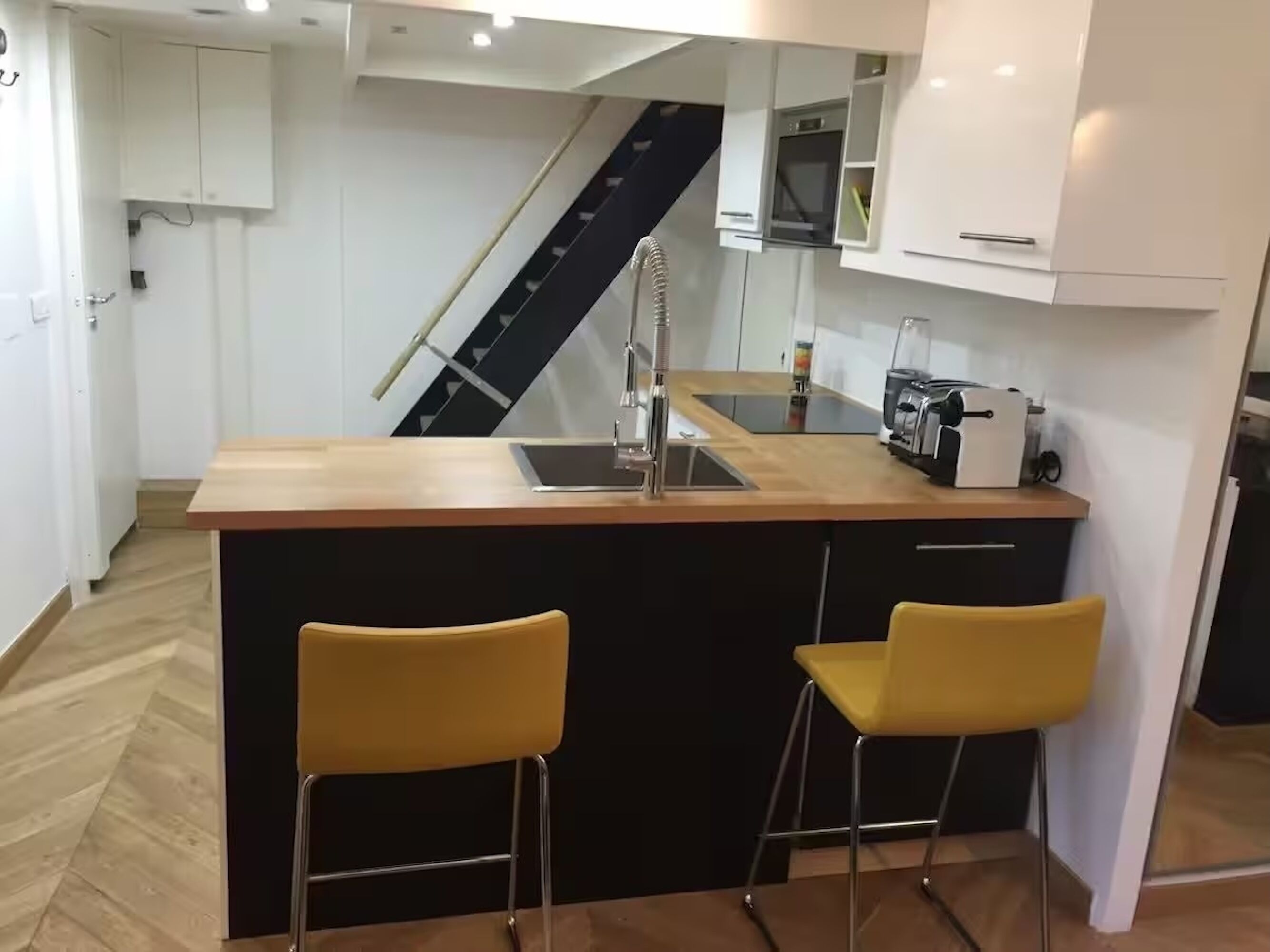 A compact kitchen with a central island, two yellow bar stools, a built-in stove, and a microwave.