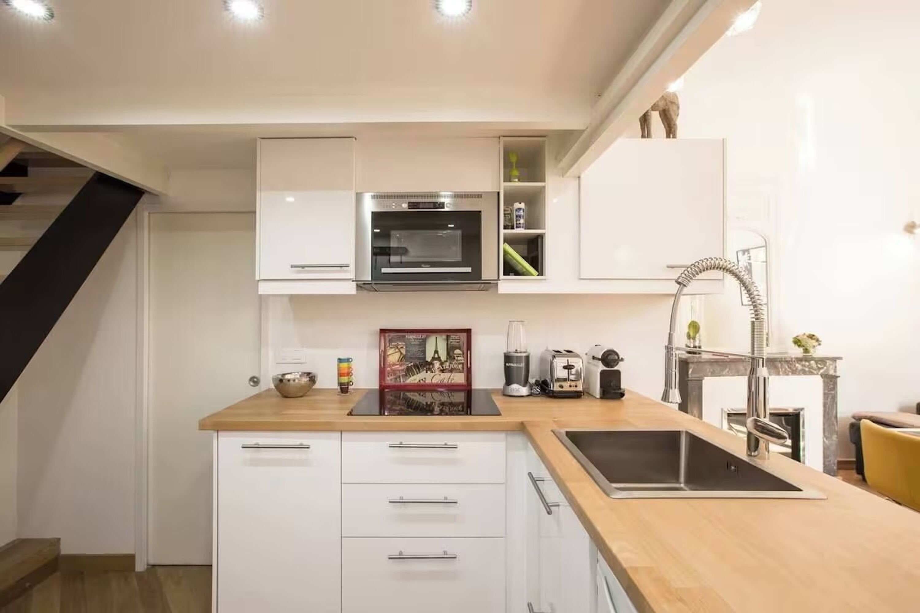 A modern kitchen with white cabinetry, a built-in oven, a sink, and a wooden countertop.