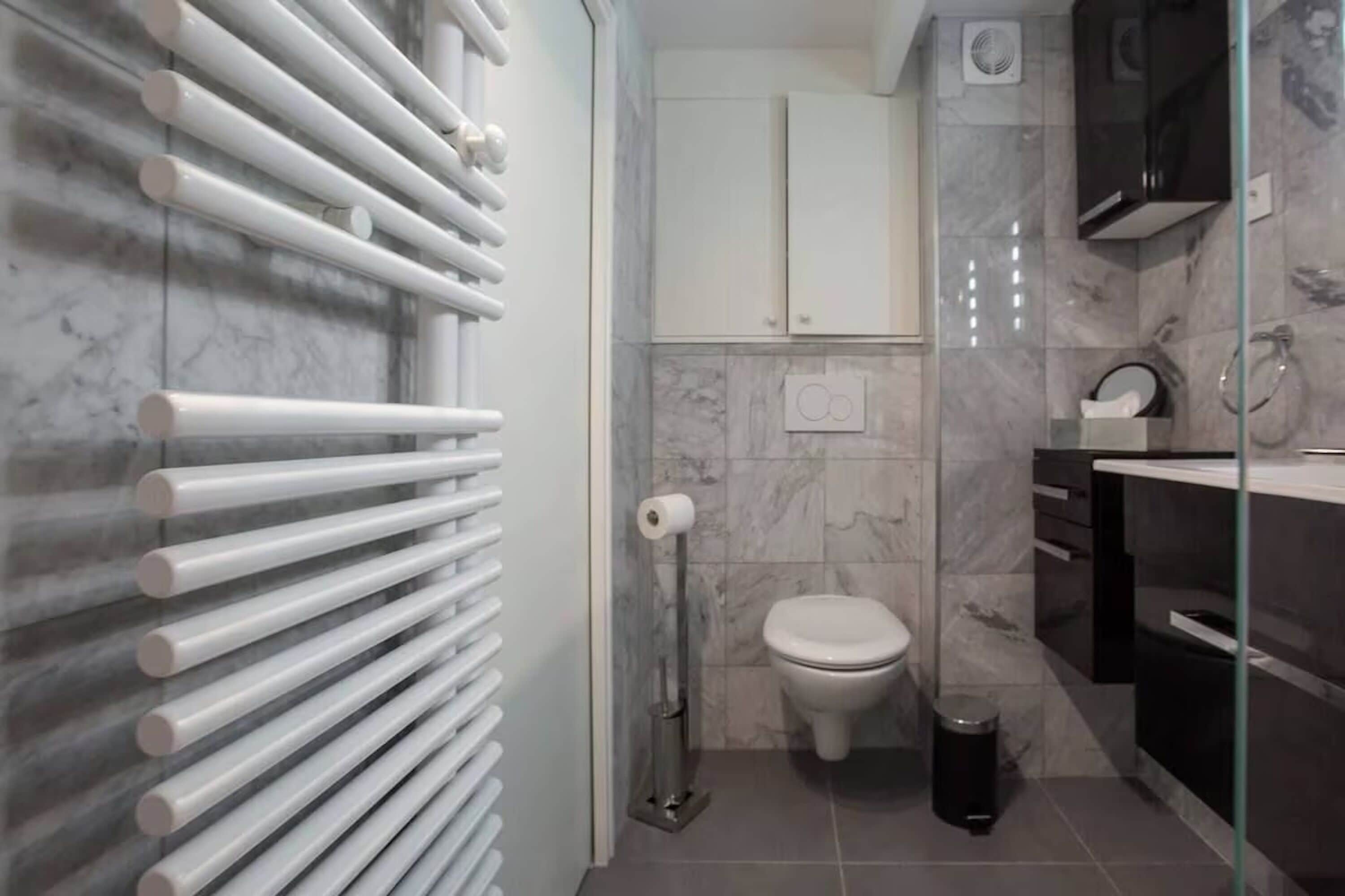 A modern bathroom with a glass shower enclosure, a white toilet, and a marble-tiled wall.